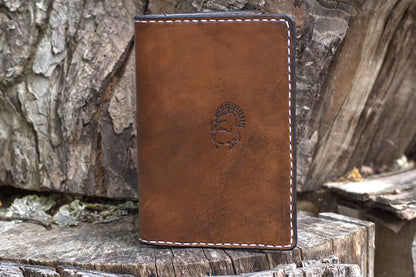 A brown leather passport wallet with white contrast stitching and an embossed profile logo. These wallets are made specifically for Old Northwest Leather's hunting journals.