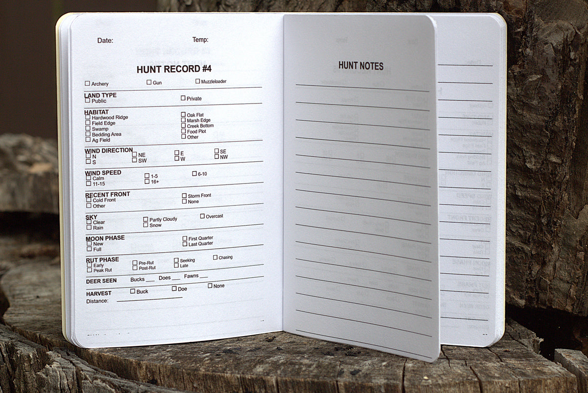 An open white hunting log notebook showing printed fields such as hunt record number, date, temperature, land type, game type, wind direction and speed, sky, moon phase, butch phase, and deer size, photographed standing on a rustic wood surface.
